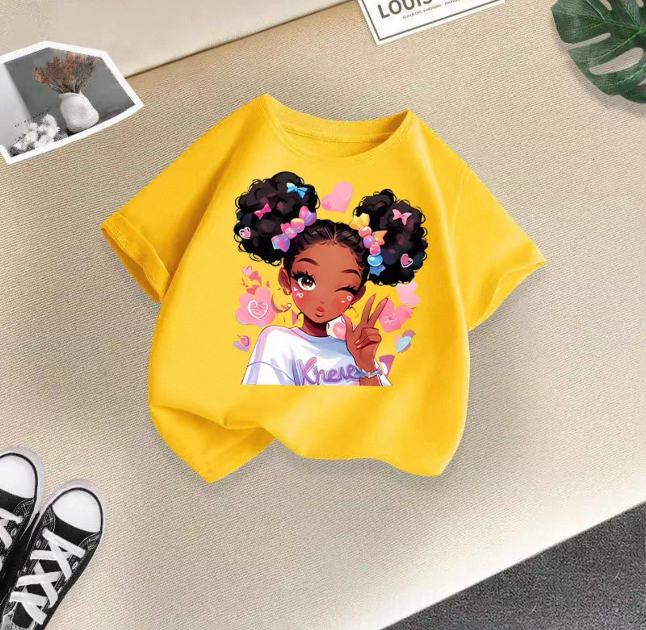 Yellow t-shirt with a graphic of a girl with styled hair on a beige surface.