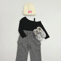 Black long-sleeve top, gray pants, white sneakers, and cream beanie with pink bow on a light gray background