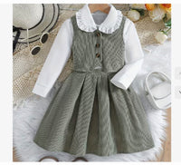 Children's outfit with gray checkered dress over white shirt on a textured surface.