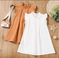Two dresses, one brown and one white, on a wooden surface with decorative items.