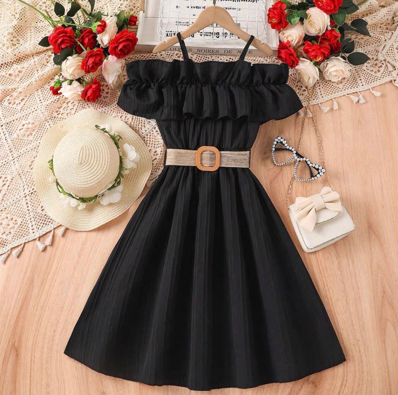 Black dress with a belt on a wooden surface with decorative items around