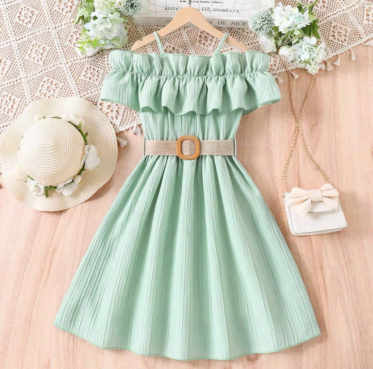Mint green dress with ruffled top and belt, placed on a wooden surface with decorative items.