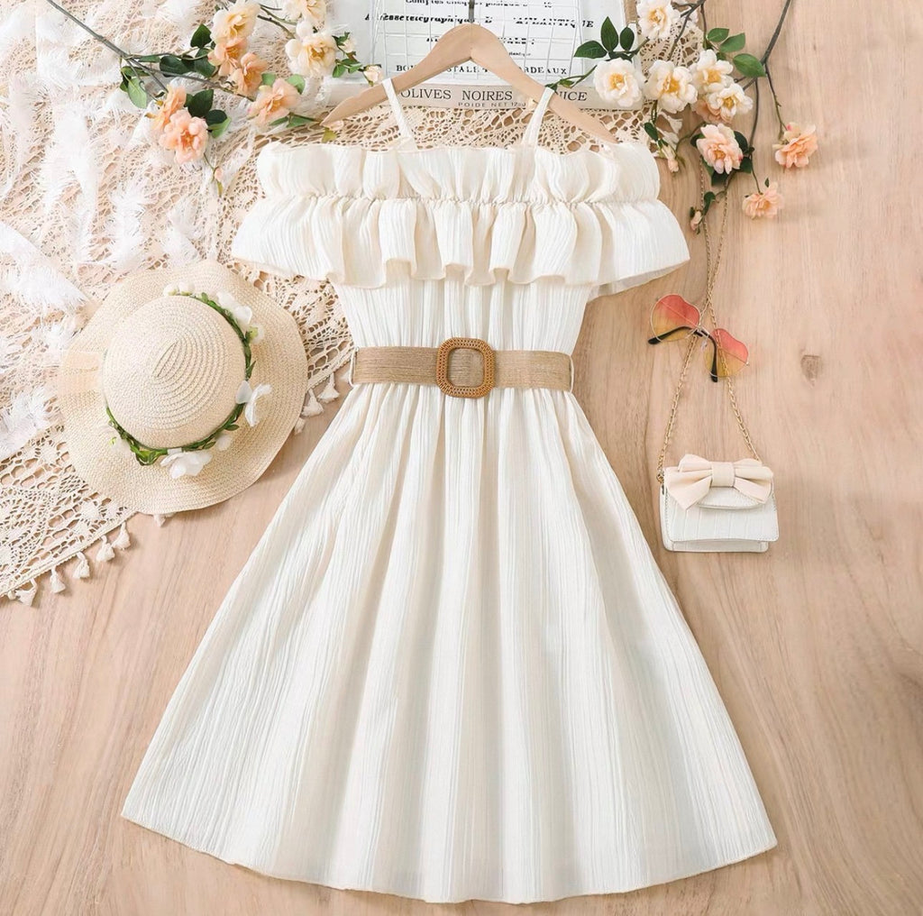 White dress with a belt, straw hat, and small handbag on a wooden surface with flowers.