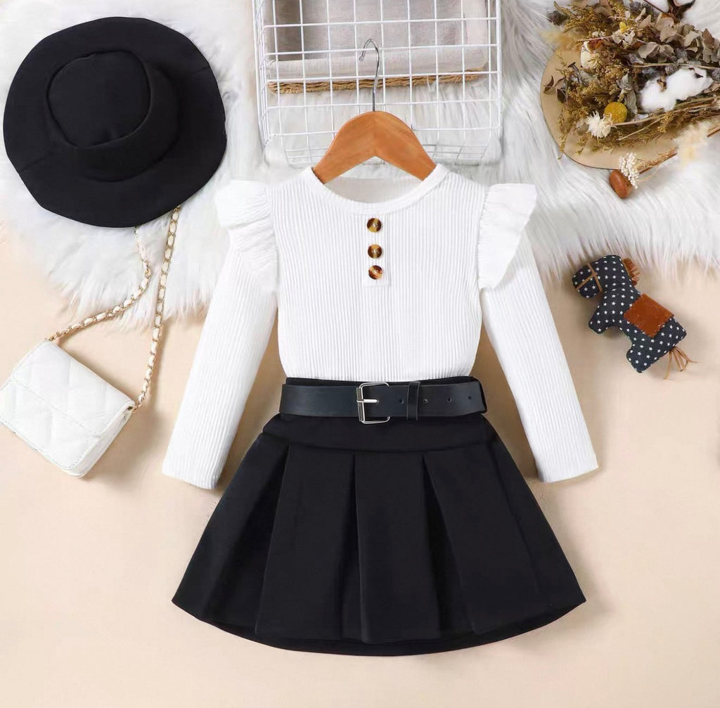 White long-sleeve top with buttons and black pleated skirt on a beige background