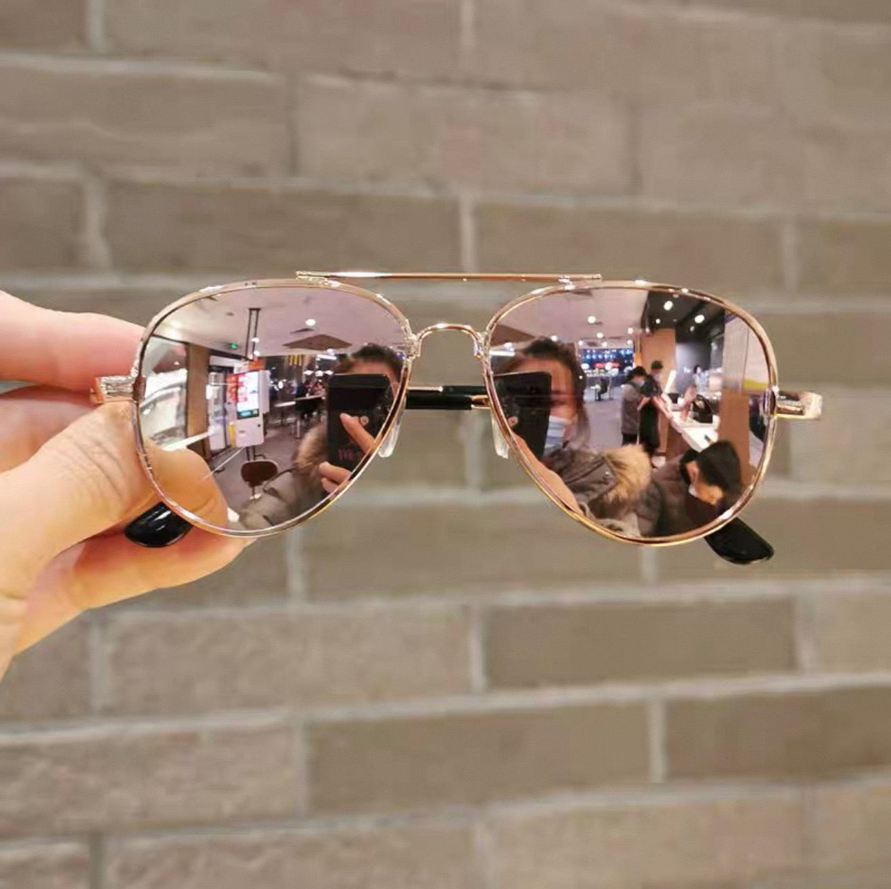 Gold-framed sunglasses held in front of a brick wall