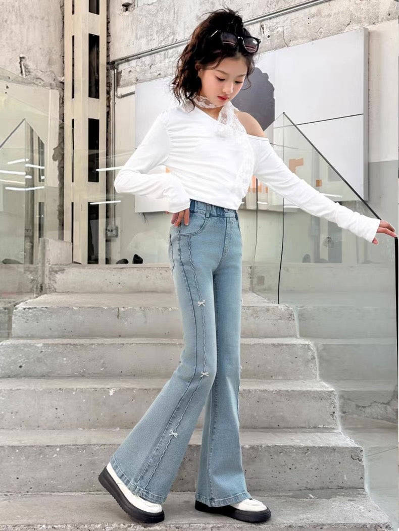 Person wearing a white off-shoulder top and light blue flared jeans standing on steps.