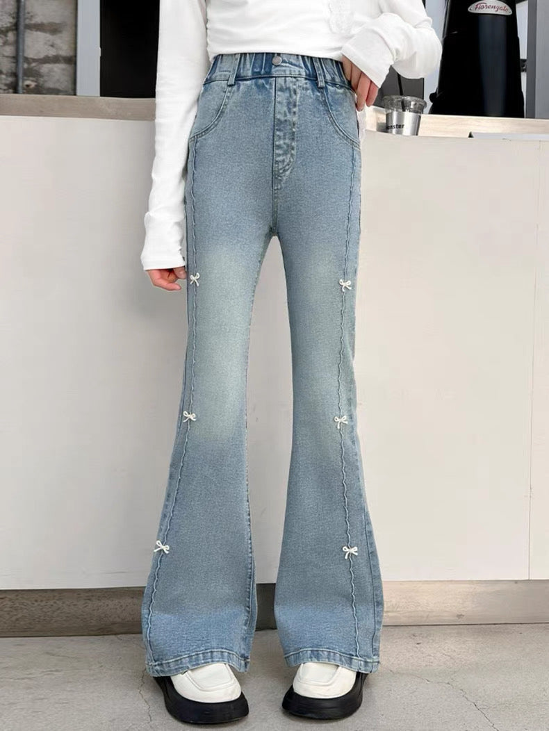 Person wearing light blue flared jeans with decorative elements indoors.