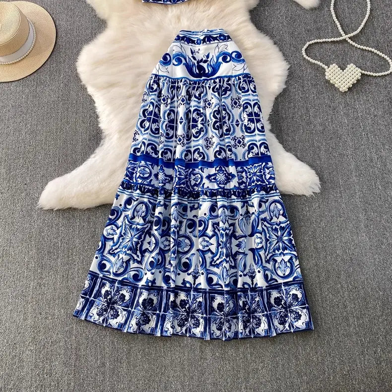 Blue and white patterned dress on a textured surface with a hat and necklace.