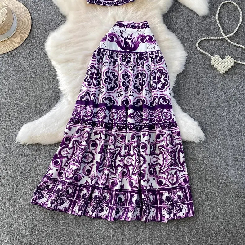 Purple and white patterned dress on a textured surface with a hat and necklace.