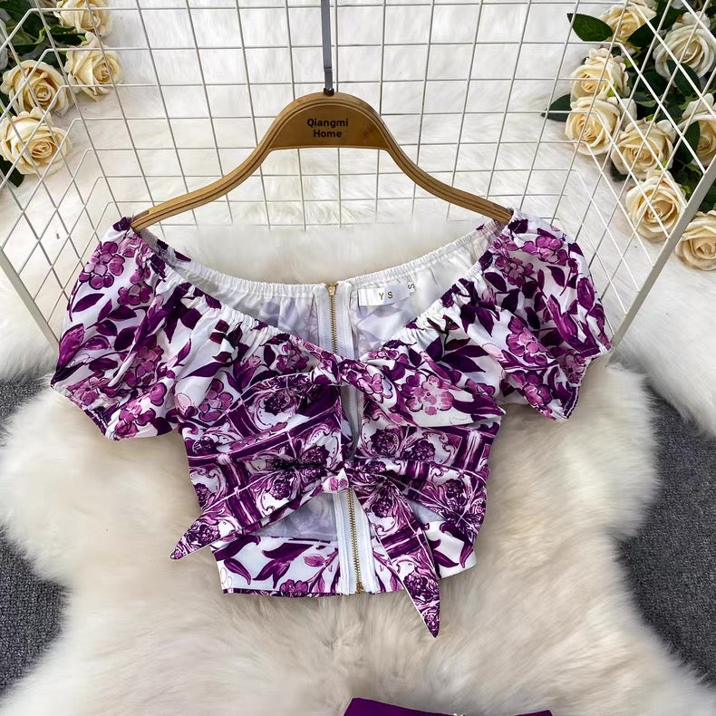 Purple floral off-shoulder top on a hanger with flowers in the background