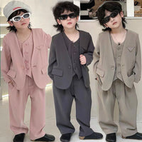Three children wearing different colored suits in a studio setting.