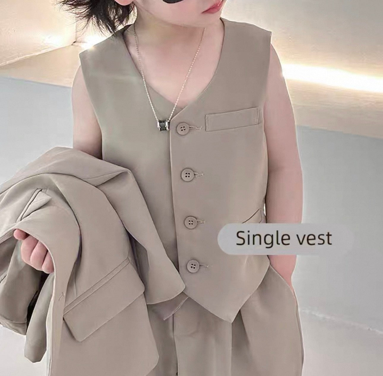 Person wearing a beige vest holding a matching jacket against a neutral background