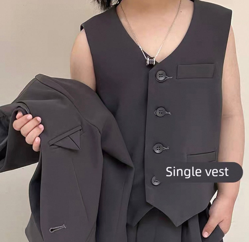 Person wearing a dark gray vest holding an additional dark gray jacket against a neutral background
