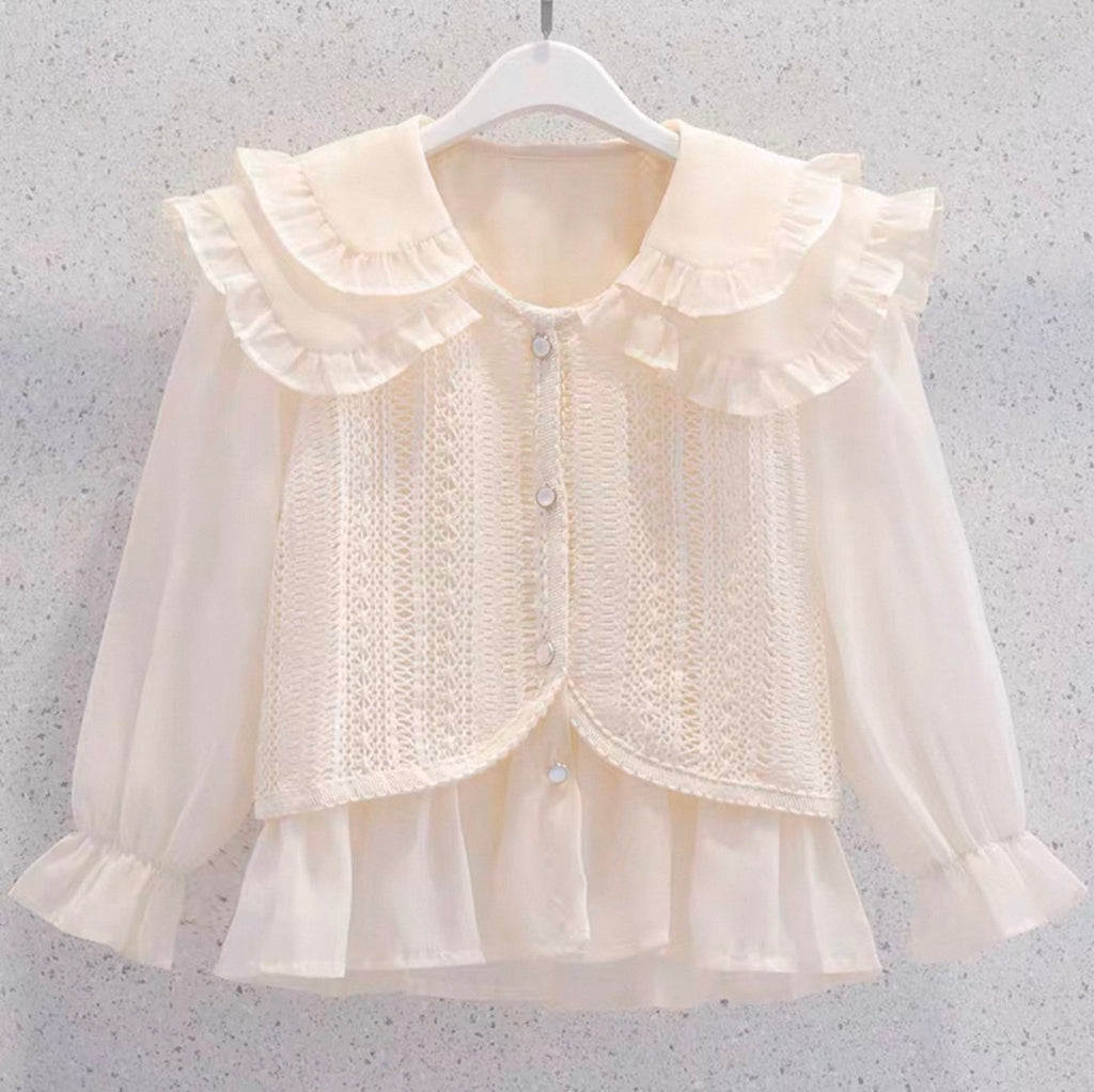 Cream-colored blouse with ruffled collar and cuffs on a hanger against a gray background