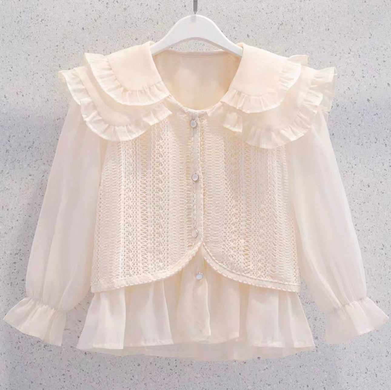 Cream-colored blouse with ruffled collar and cuffs on a hanger against a gray background