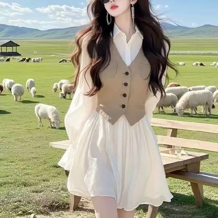 Woman in a white dress with a beige vest standing in a pastoral setting with sheep and mountains.