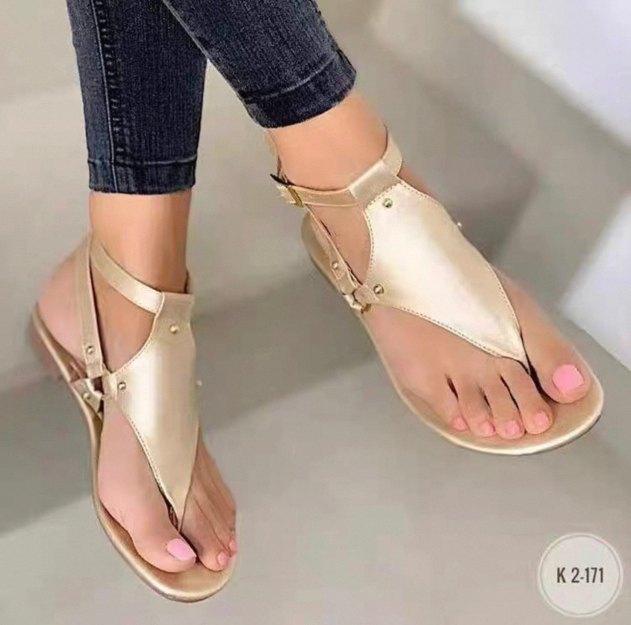 Gold sandals worn with rolled-up jeans on a neutral background