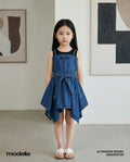 Young girl wearing a blue denim dress standing in a room with abstract art on the walls.